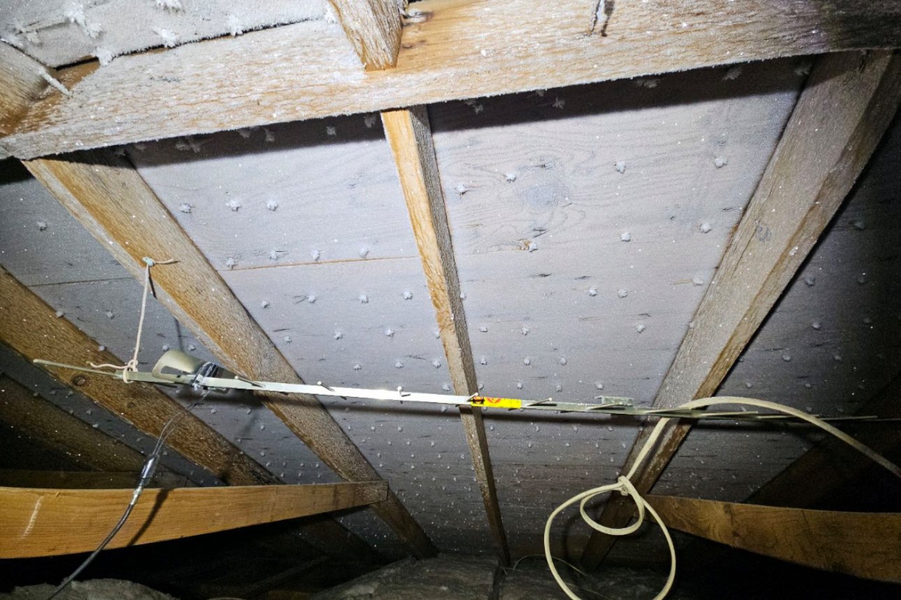 Frost crystals on the nail tips and roof sheathing inside an attic, lit by a flashlight